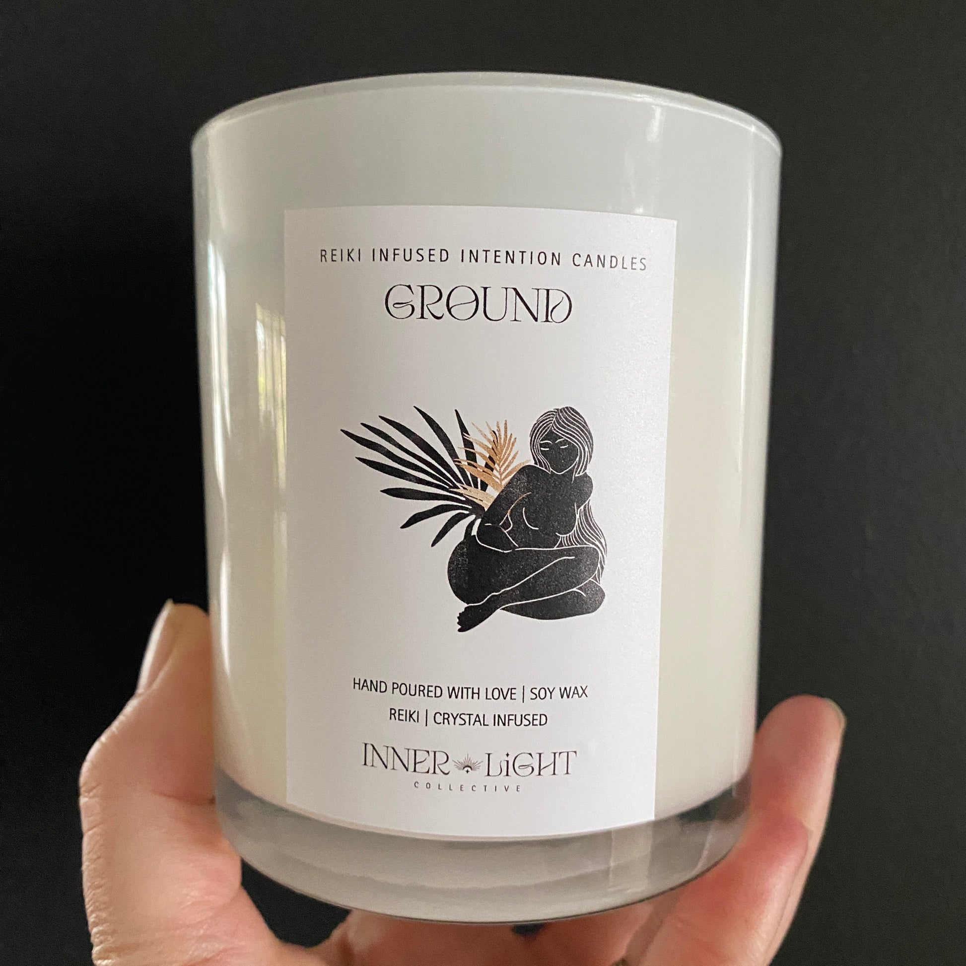 a hand holding a white glass candle vessel. woman on front, palm fronts, grounding image of grounding candle