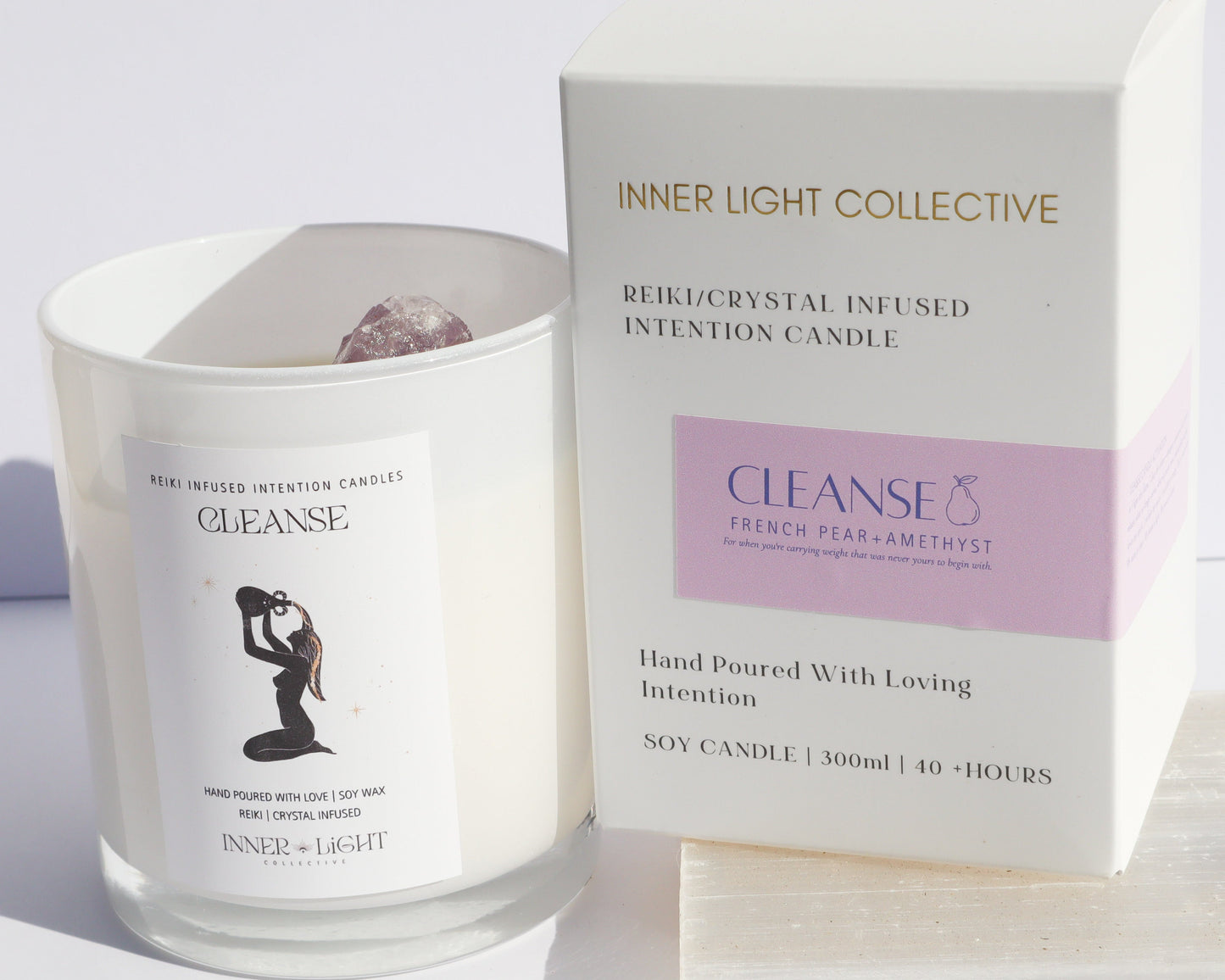 A glass jar candle labeled 'CLEANSE' by Inner Light Collective stands beside its white product box with a lavender panel. The box reads 'INNER LIGHT COLLECTIVE' and 'CLEANSE' and is photographed on a light neutral surface against a white background.
