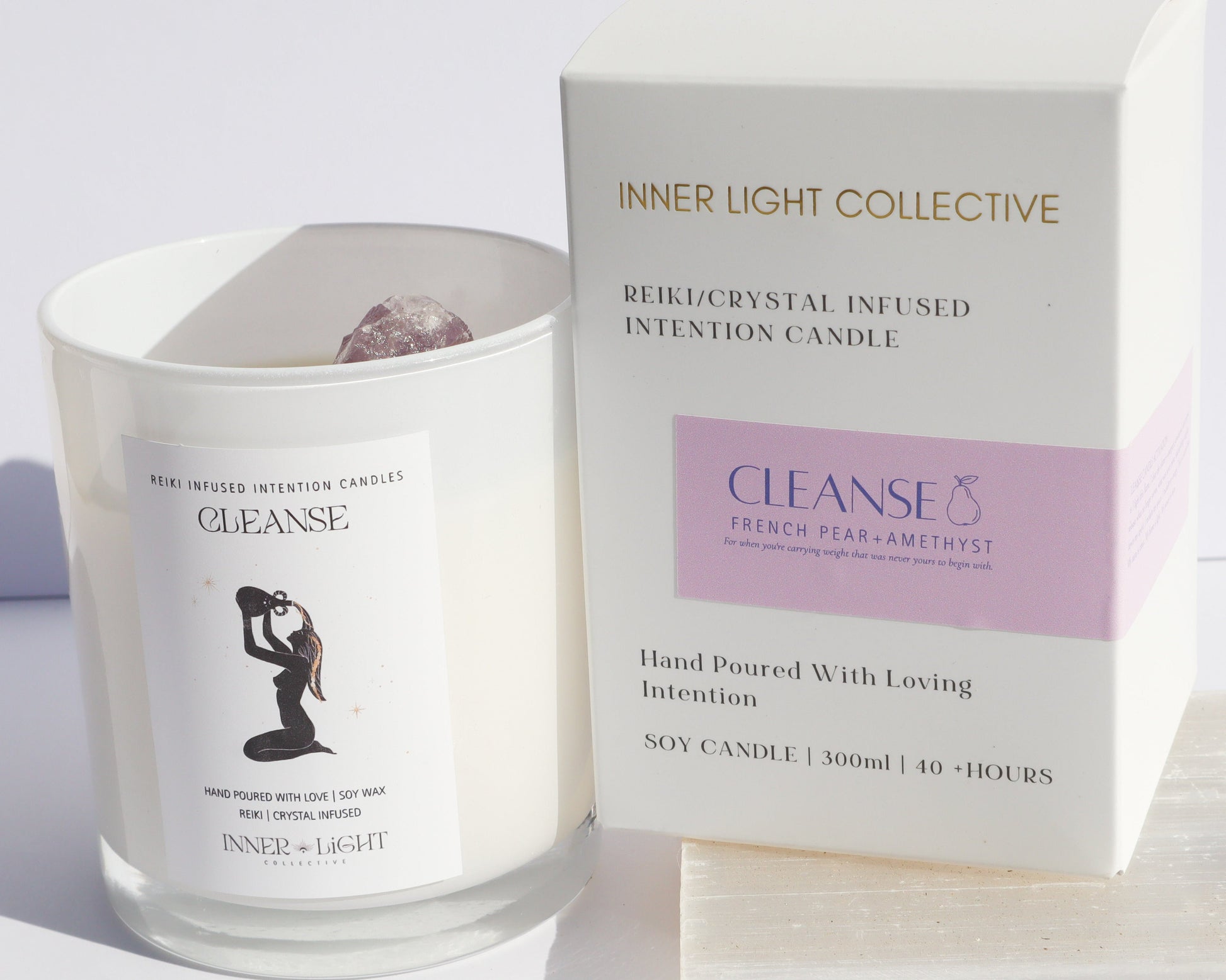 A glass jar candle labeled 'CLEANSE' by Inner Light Collective stands beside its white product box with a lavender panel. The box reads 'INNER LIGHT COLLECTIVE' and 'CLEANSE' and is photographed on a light neutral surface against a white background.